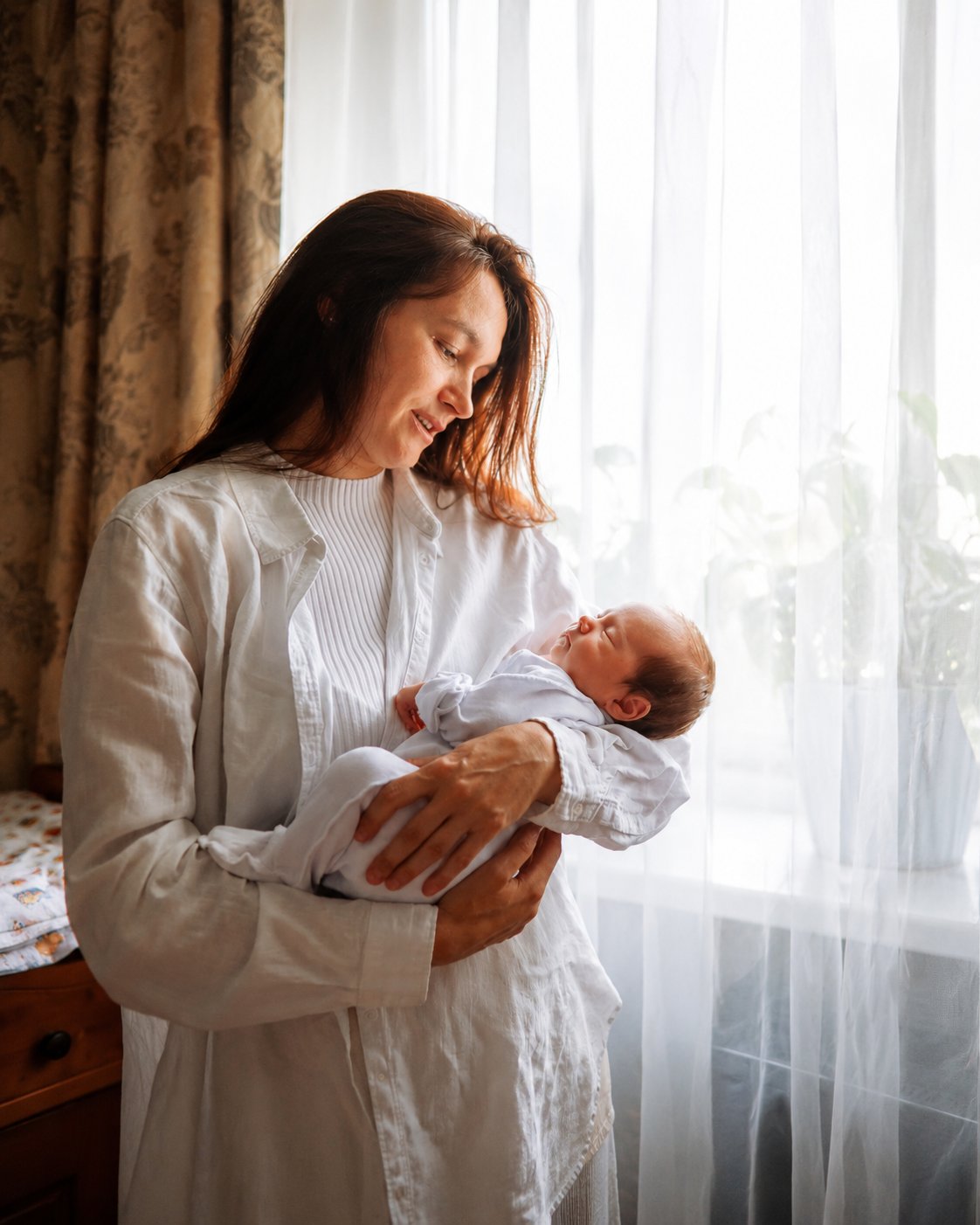Mother holding a newborn beside a bright window